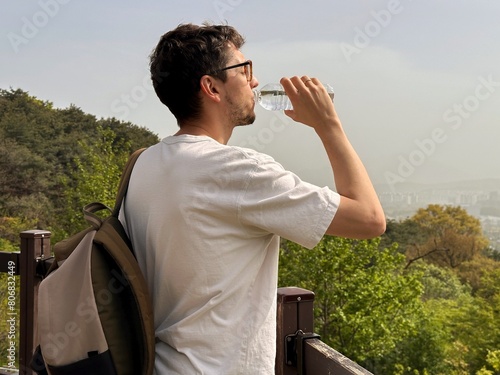 Tourist with a backpack drinks water from the bottle on the observation deck