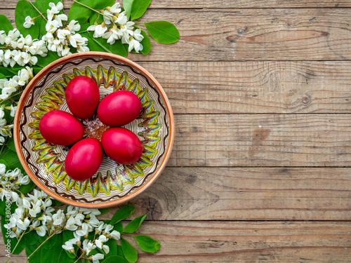 red easter eggs in decorated clay plate framed by acacia flowers and leaves