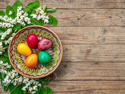 colored easter eggs in decorated clay plate framed by acacia flowers and leaves