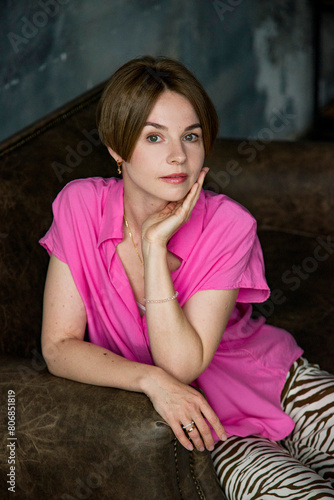  closeup portrait of beautiful blonde woman in pink shirt sitting on the sofa and touching her face by hands in the dark room