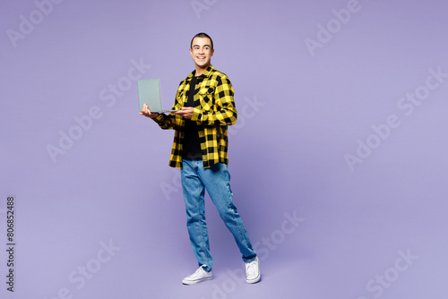 Full body side view young IT middle eastern man wear yellow shirt casual clothes hold use work on laptop pc computer isolated on plain pastel light purple background studio portrait Lifestyle concept
