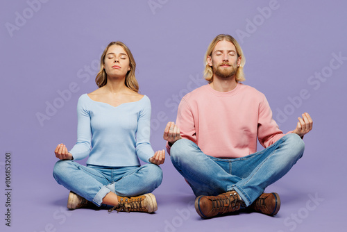 Full body young couple two friend family man woman wear pink blue casual clothes together sitting hold hands in yoga om aum gesture relax meditate try to calm down isolated on plain purple background