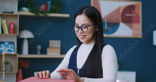 Charming Chinese female finishing work for day. Pressing keys on keyboard. Closing laptop with one hand. Looking directly at camera and showing with hand gesture heart symbol. Modern apartment. photo