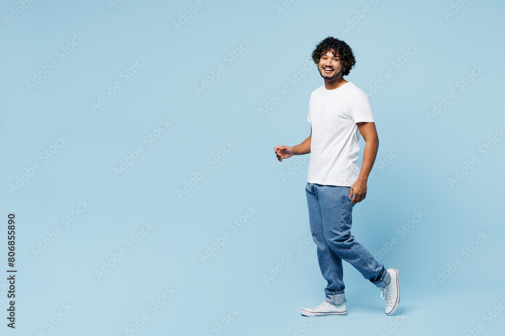 Full body side profile view young smiling cheerful happy Indian man he wear white t-shirt casual clothes walk go isolated on plain pastel light blue cyan background studio portrait. Lifestyle concept. Full body side profile view young smiling cheerful happy Indian man he wear white t-shirt casual clothes walk go isolated on plain pastel light blue cyan background studio portrait. Lifestyle concept.