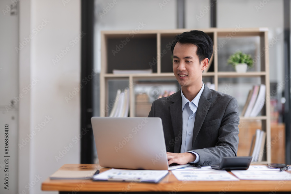 Young Asian man working on laptop in modern office analyze accounting, report real estate investment information. Young Asian man working on laptop in modern office analyze accounting, report real estate investment information.