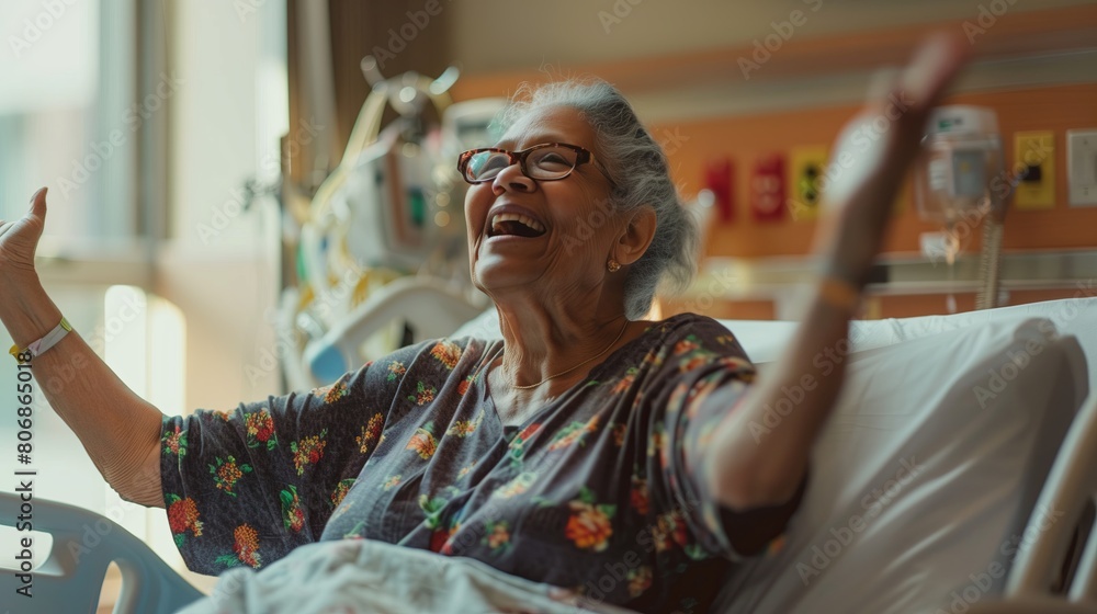 Obraz premium Portrait of a happy elderly woman sitting in a hospital room and raising her hands up.