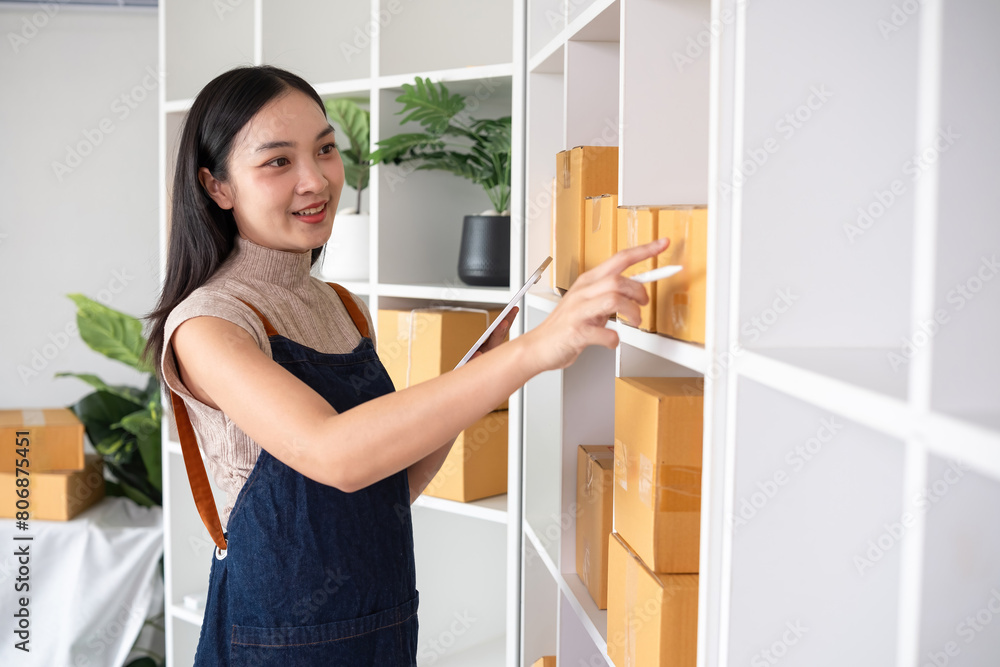 A small SME business owner checks an order and writes shipping information on a cardboard box in his home office to prepare for delivery. A small SME business owner checks an order and writes shipping information on a cardboard box in his home office to prepare for delivery.
