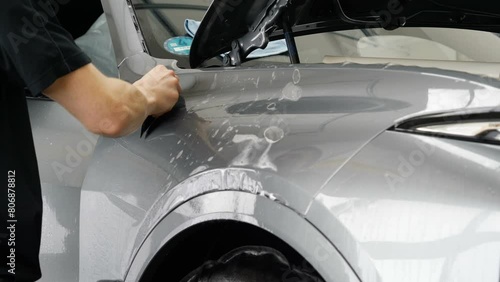 Close up of paint protection film installation on front bumper of modern luxury car. PPF is polyurethane film applied to car surface to protect the paint from stone chips, bug splatter, and abrasion.