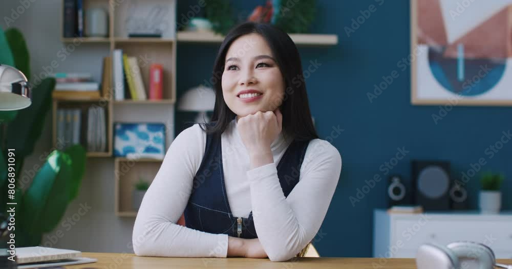 Camera closing in on Asian female. Girl sitting in front of desk. Beginning dreaming of something. Afterwards looking directly at camera while smiling. Placing hand under her chin. Camera closing in on Asian female. Girl sitting in front of desk. Beginning dreaming of something. Afterwards looking directly at camera while smiling. Placing hand under her chin.