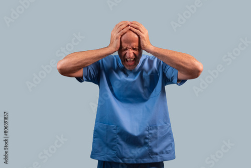 Portrait of a physiotherapist in light blue gown and hands on head.