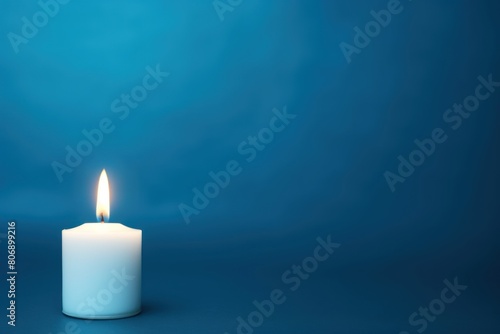 Blue background with white thin wax candle with a small lit flame for funeral grief death dead sad emotion with copy space texture for display 