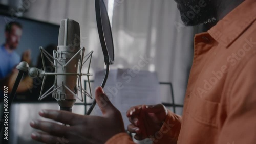 Close-up of hands of African American male voice-over actor dubbing emotional movie scene of couple having violent quarrel, reading lines from cue sheet, gesticulating, while working in studio