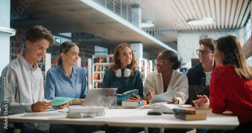 Diverse Group of Students Collaborating on a Project in a Modern Library. Young Men and Women Using Laptops and Books, Engaging in Group Discussion and Learning Together. © Gorodenkoff