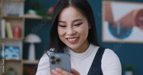Beautiful Asian woman using her personal phone for remote communication from home. Satisfied young girl typing fast response or message to her boyfriend on smartphone. Positive online chat. photo