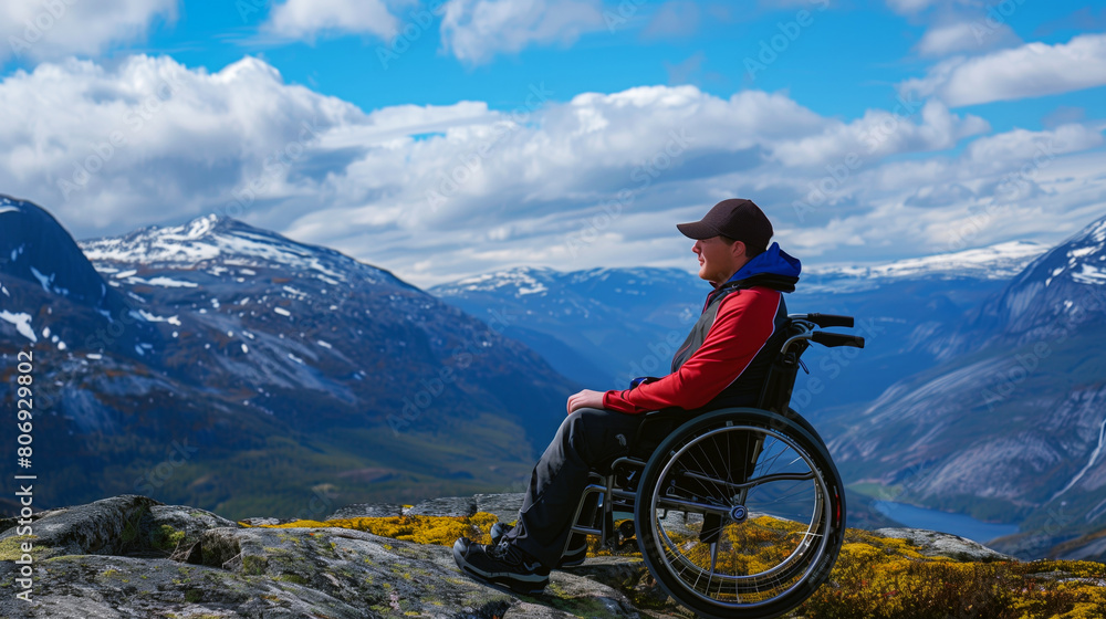 Fototapeta premium A man in a wheelchair enjoys a panoramic view of majestic mountains and a serene lake.