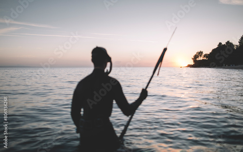 Selective focus of spearfisherman holds speargun and watch the sunset photo