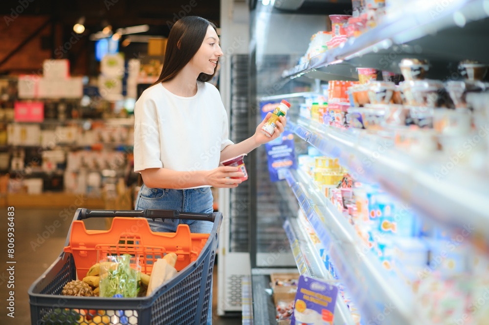 Obraz premium Young smiling happy woman 20s in casual clothes shopping at supermaket store with grocery cart