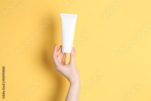 Woman holding tube of cream on yellow background, closeup. Space for text © New Africa