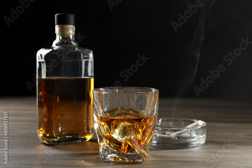 Alcohol addiction. Whiskey in glass, bottle, cigarettes and ashtray on wooden table