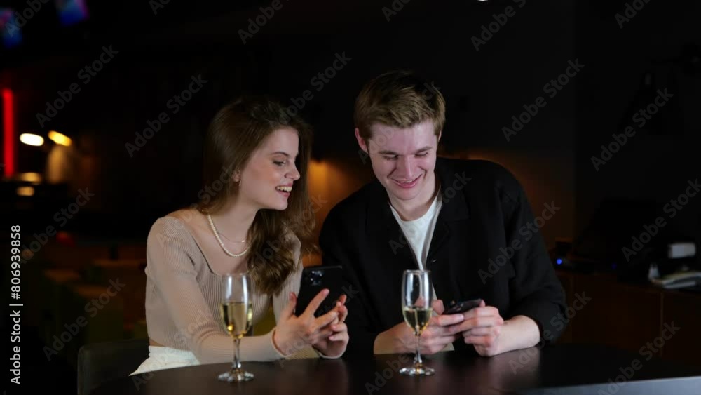 Happy young man and woman sitting in the restaurant while using smartphones and reading message. Glasses of champagne on the table. Lifestyle, relationship, date concept. Real time. Happy young man and woman sitting in the restaurant while using smartphones and reading message. Glasses of champagne on the table. Lifestyle, relationship, date concept. Real time.