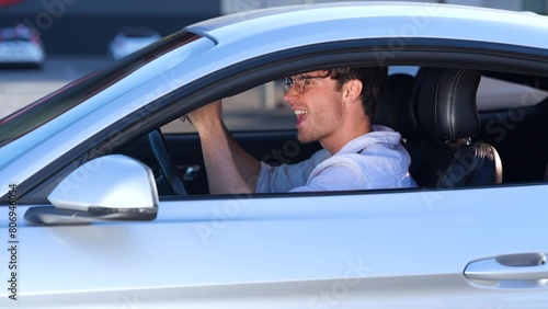 Happy guy in glasses enjoying his car trip while singing song and dancing, driving in the city. Transport and lifestyle concept. Real time © Nataliya