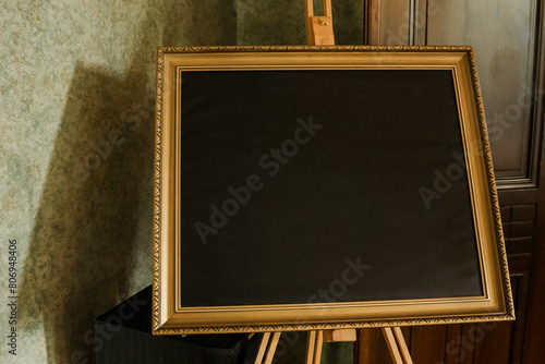 Blank blackboard with gold frame on the table in room.