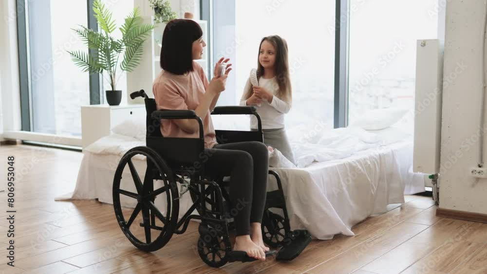 Mother with disability sings with her adorable little daughter using combs instead of microphones while sitting on bedroom. Happy family having fun on a weekend morning. Mother with disability sings with her adorable little daughter using combs instead of microphones while sitting on bedroom. Happy family having fun on a weekend morning.