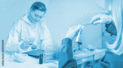 Woman laboratory assistant. Girl employee medical laboratory. Scientist holds test tube for drug synthesis. Hands with reagents. Woman doctor is sitting at lab table. Chemist in white protective suit photo