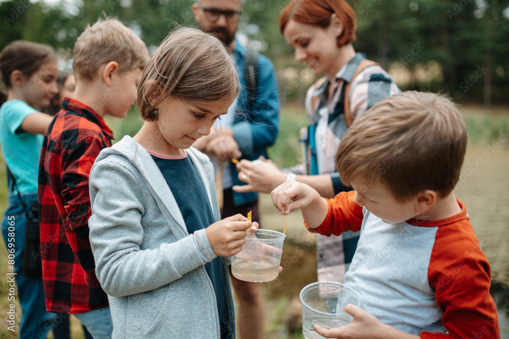 Young students analyzing water quality, ph level with indicator strips during biology field teaching class. Female teacher during outdoor active education. Young students analyzing water quality, ph level with indicator strips during biology field teaching class. Female teacher during outdoor active education.