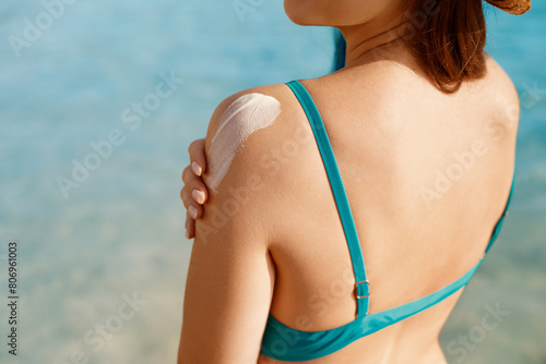 Beautiful Woman in Bikini Applying Sun Cream on Tanned Shoulder. Sun Protection. Skin and Body Care. Girl Using Sunscreen to Skin. Portrait Of Female Holding Suntan Lotion and Moisturizing Sunblock