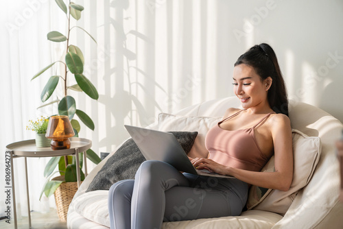Asian beautiful lady with black long hair work at the notebook sit down on the sofa at home . Check on oline shops for sales - technology woman concept for alternative office freelance photo