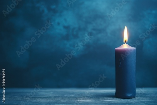 Indigo background with white thin wax candle with a small lit flame for funeral grief death dead sad emotion with copy space texture for display 