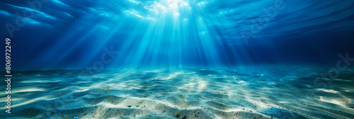 Underwater seascape showing a sandy seabed with sunlight streaming through the water. photo