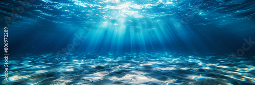Underwater view of sun rays penetrating clear blue ocean water and illuminating the sandy bottom. photo