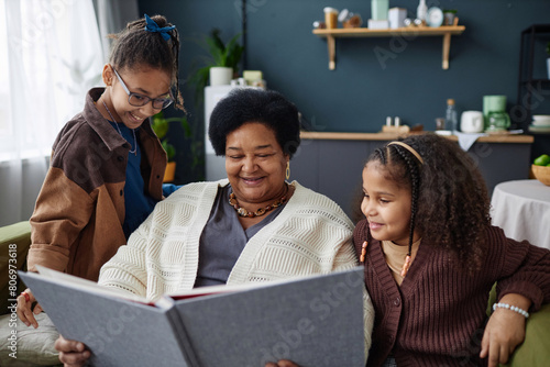 Portrait of smiling senior African American woman with two children looking at family photo album together at home