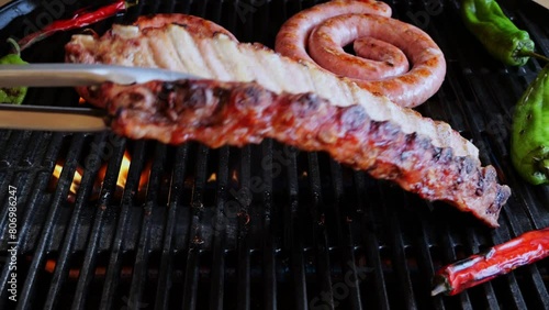 Chef turns over pork ribs On Grill. Cooking natural sausage on grill. Slow motion. Close up
