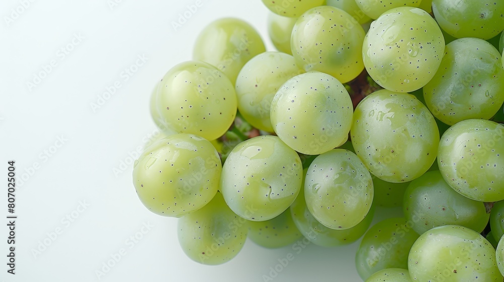 A collection of green grapes atop a white table, adjacent to a piece of broccoli on the same table A collection of green grapes atop a white table, adjacent to a piece of broccoli on the same table