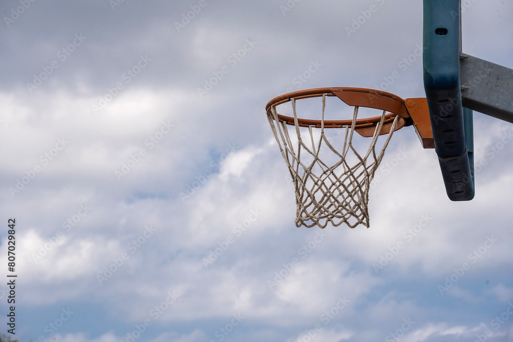 A Shot from the side of a basketball hoop with blue sky with clouds in the background and space for text.