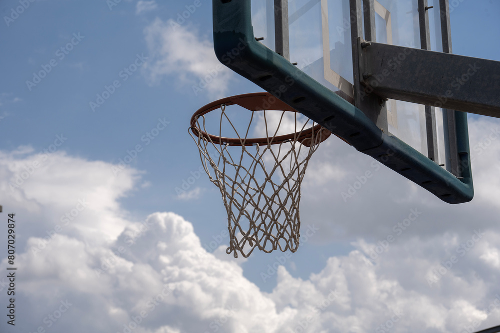 A Shot from the side of a basketball hoop with blue sky with clouds in the background and space for text.