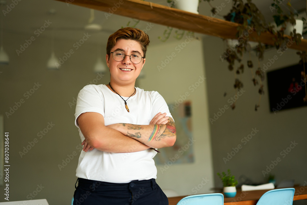 custom made wallpaper toronto digitalConfident Gen Z transgender person stands in modern office, arms crossed, smiling. Inclusive workplace with natural light, plants. Casual work attire, LGBTQ pride, authenticity at work reflected.