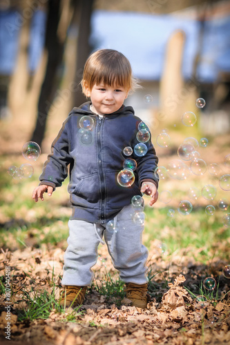 Happy smiling cute toddler delights in chasing floating soap bubbles, bathed in sunlight amidst nature. Love and family concept
