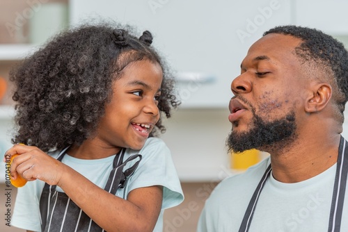 african afro hair black kid Cute taste oranges citrus sour flavour on lips mouth with daddy in kitchen. back african daughter kid afro hair and daddy frowning face for taste is sour of sliced orange photo