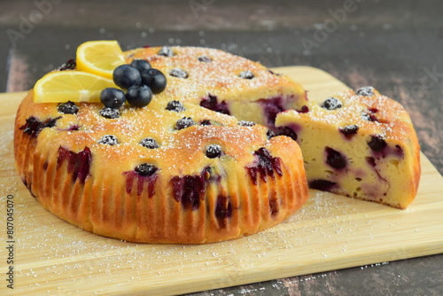 Lemon blueberry cake with powdered sugar on top on the board on a wooden background. 
