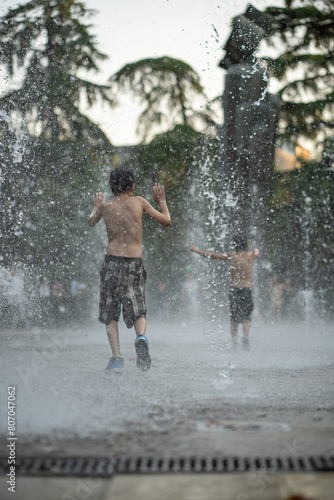 Children playing happily in city fountain  seeking relief from scorching summer heat. Joyful kids delight in refresh water  finding respite from sultry  enjoy carefree escape from hot sweltering day.