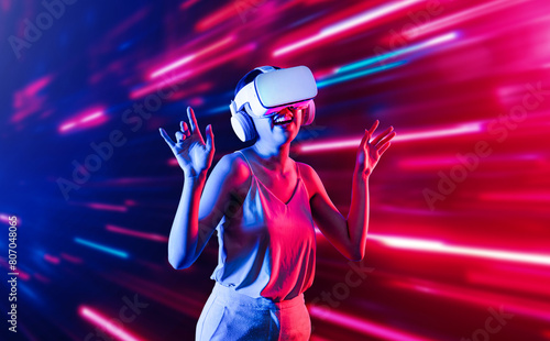 Smart female standing surrounded by neon light wearing VR headset connecting metaverse, future cyberspace community technology. Elegant woman enjoy dancing wavering body and sing song. Hallucination.