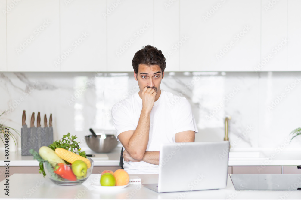 Young man sits at the table and looking at laptop. Online training and food blogger concept Young man sits at the table and looking at laptop. Online training and food blogger concept