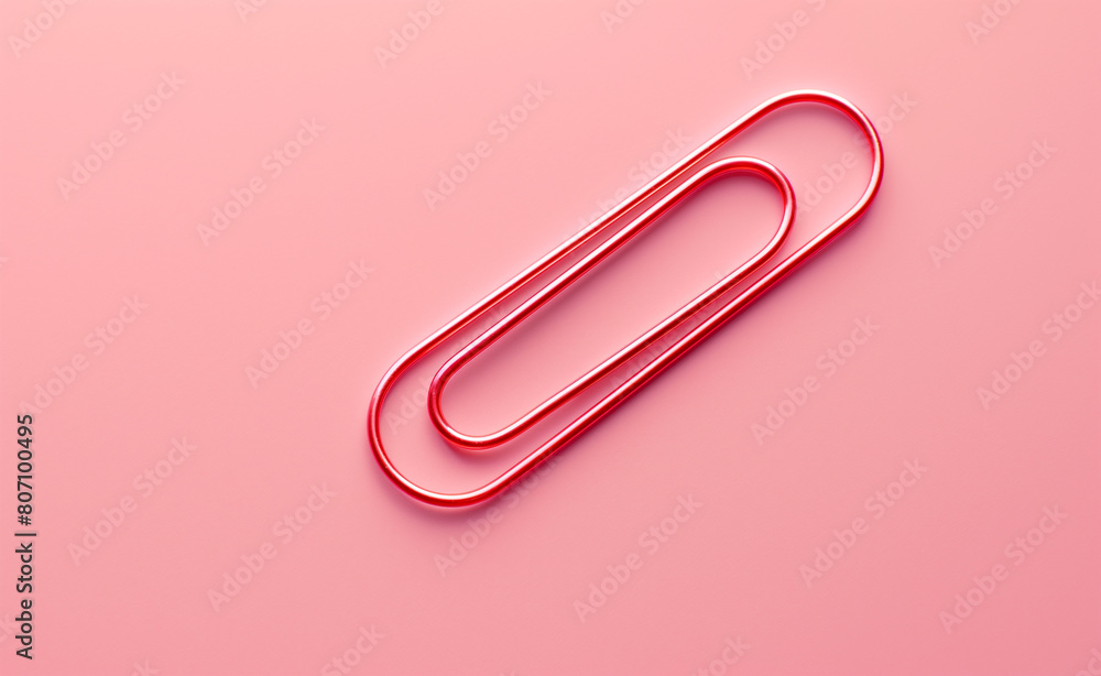 Single red paper clip lying on a soft pink background Single red paper clip lying on a soft pink background