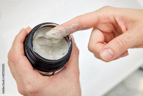 female hand takes a clay face mask from a jar. home spa. close-up