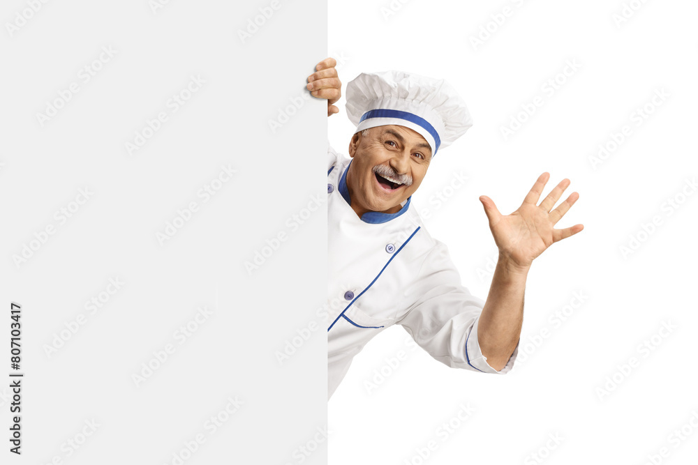 Mature male chef in a uniform waving from behind a blank panel Mature male chef in a uniform waving from behind a blank panel