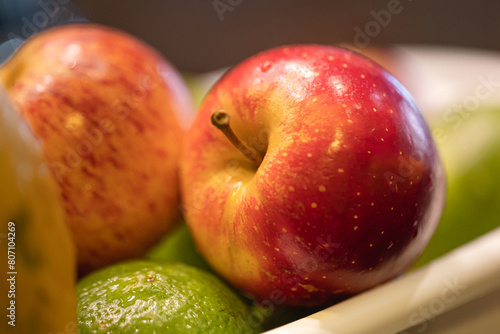 Um cesto plástico com frutas higienizadas com uma maçã vermelha em destaque. Macrofotografia.
